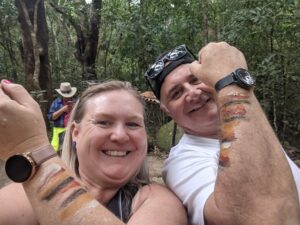 Donna next to traveller at Mossman Gorge with fists raised showing ochre paint on forearms